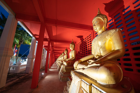 Several golden statues of Buddha statues in meditation posture are lined up in a corridor and...