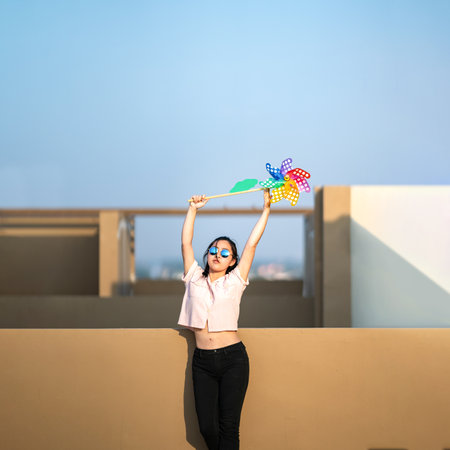 Asian woman posts and play Windmill Toy colourful rainbow colour on the building rooftop in sunset time.の写真素材