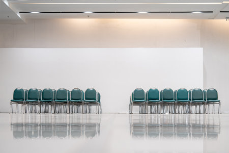 Many empty green leather chairs in a wide hall room, lights on. A floor reflect the objects. Give a feeling of emptiness.の写真素材