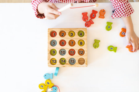 Topview, flatlay of Kid's hands are playing and finding the matched number in the wooden magnetic fishing game,の写真素材