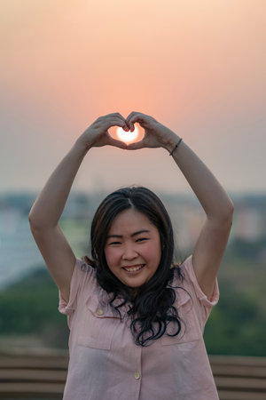 Asian Chinese Thai woman plays with the sun shape on rooftop in twilight time.の写真素材