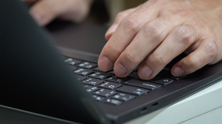 A man is typing on a black laptop provided with Thai English keyboard.
