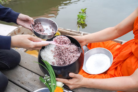 The monk was Holding monk's alms-bowl, between Thai Local people make merit by offering food rice to the monk who in a vintage wooden boat in the morning.の写真素材