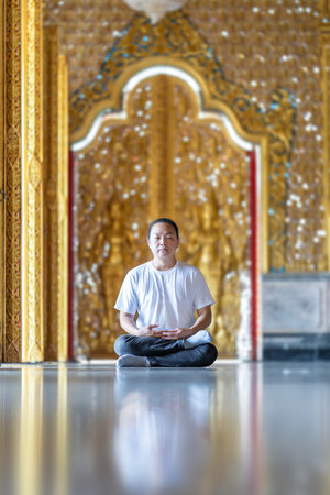 Asian Man meditates on the ground with reflection in the sunlight pouring into the temple church...