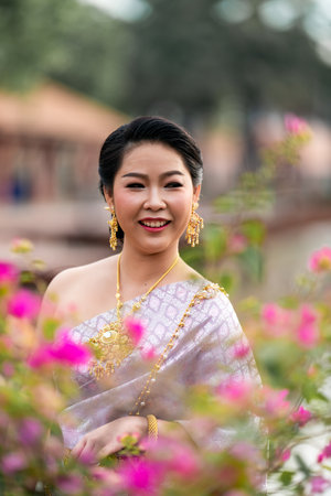 A woman in a traditional Thai costumes is standing on the wooden bridge while being taken a portrait photo shooting.の写真素材