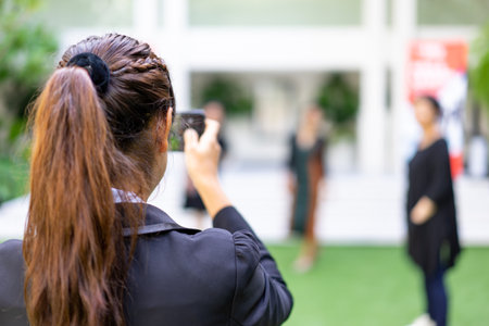 A woman standing with her back taking a picture with a mobile phone.