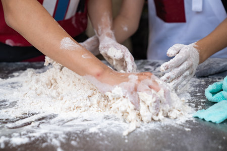 Two skilled Asian men showcase their expertise as they deftly work together, their four hands skillfully kneading and threshing flour on aluminum plate, in preparation for crafting freshの写真素材