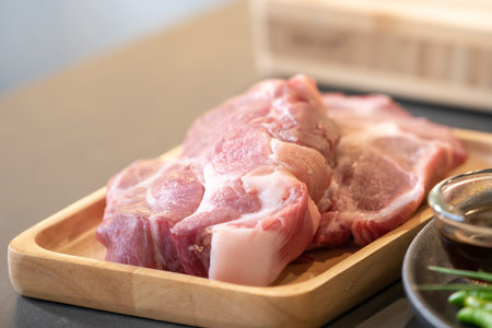 Raw Pork is prepared for Cook, It is on wood plate on black granite kitchen counter tabletop, shot by studio light.の写真素材
