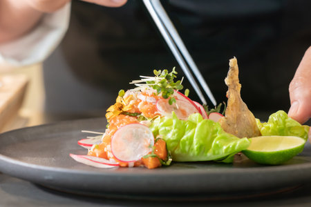 Tweezers chef in Chef's hand decorates Spicy Salmon Salad by micro herb on the food.の写真素材