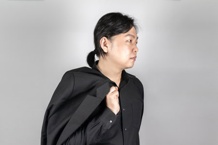 Asian Man in black suit is standing in front of light gray background.の写真素材