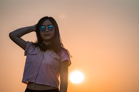 Asian glasses long hair girl is silhouette posting for camera shooting on the rooftop, top of building in twilight sunset time.の写真素材