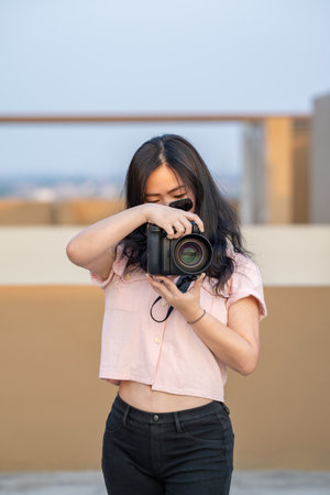 Amateur sunglasses Asian Woman take a photo with professional mirrorless camera at outdoor blue rooftop building in twilight time.の写真素材