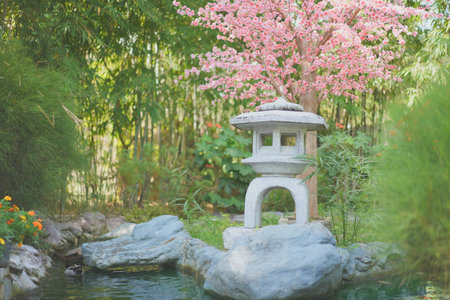 Japanese garden style with a reflection steam and artificial Sakura flower behind the Japanese rock lantern at noon.の写真素材