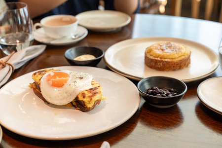 A fried sunny-side-up egg topped with black pepper sits beautifully on melted cheese toast, served...