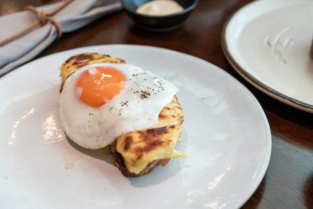 A fried sunny-side-up egg topped with black pepper sits beautifully on melted cheese toast, served...