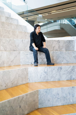 Asian Man in Black cardigan and polo shirt sits on the white grand marble stairs in the grandstand...