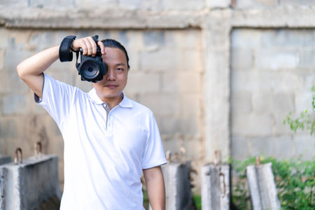 Professional Asian Chinese - Thai Camera man posture and focus in viewfinder and LED screen on mirrorless camera medium format in construction concrete area.の写真素材