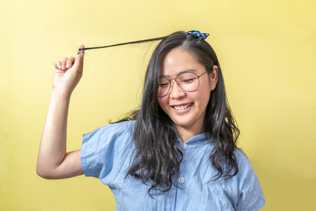A young asian girl touch her hair smoothly with a big smile on her face in front of yellow...