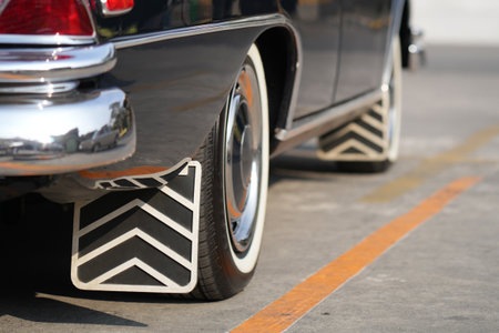 The rear wheel of a vintage black car with a classic rubber mudflap, a practical feature that blocks...