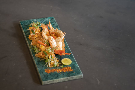 Lobster Pad Thai is served with yellow noodle, fried tofu, cress, bean sprouts, chilli power, garlic chives, and lime put on a rectangular plate.の写真素材