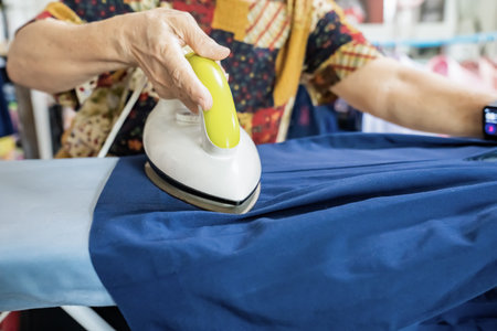 Senior citizens ironing student skirt and clothing in a house.の写真素材