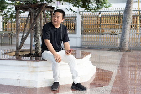 A traveler takes a rest at the temple courtyard, listening to music and enjoying the calm surroundings before continuing the journey.の写真素材
