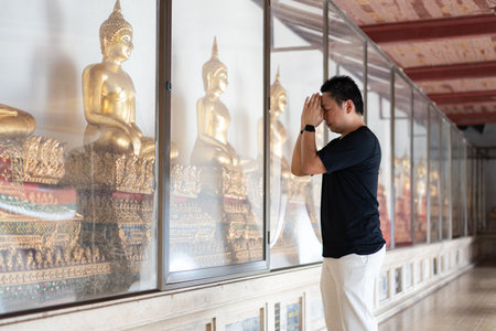 A man pays respect to the golden Buddha statues inside a temple, representing the cultural beauty of faith and traditional Thai spirituality.の写真素材