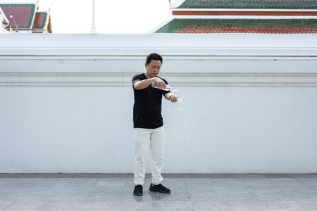 A man gently pours water over his hands, symbolizing cleansing, purity, and mindfulness against a minimalist temple wall background.の写真素材