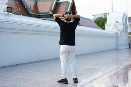 A man stands still with his hands behind his head beside a temple wall a silent pause that captures calm, awareness, and release from the noise of the world.の写真素材