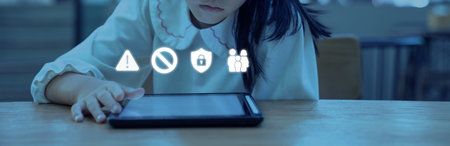 Soft blue light reflects on the tablet as the child taps the screen while safety icons appear above concerns about online risks and the need for careful guidance.の写真素材