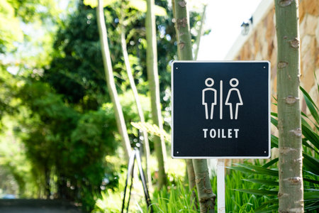 A black restroom sign stands among green plants along an outdoor walkway, displaying male and female icons with the word toilet printed below.の写真素材