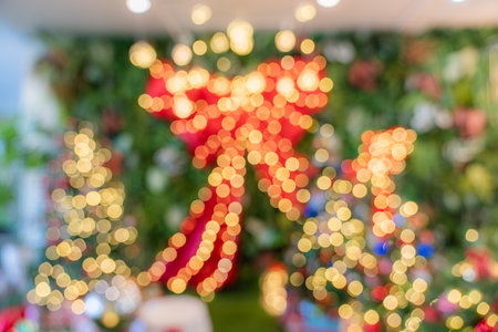 The image features blurred holiday lights forming round yellow and red bokeh shapes, with a large red bow and decorative trees soft in the background.の写真素材