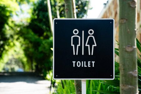 A black restroom sign stands among green plants along an outdoor walkway, displaying male and female icons with the word toilet printed below.の写真素材