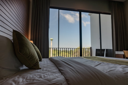 A hotel room with wooden wall paneling and soft lighting displays a large bed with white bedding and green pillows, along with bedside tables holding mounted lamps.の写真素材