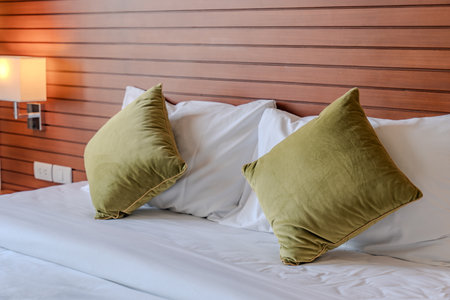A bed with white sheets and green pillows sits against a wooden panel wall, with two wall lamps and small side tables creating a simple layout.の写真素材