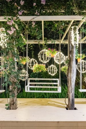 A white garden pavilion glows with hanging lights shaped like spheres and stars, while flowers and vines decorate the structure in the quiet night garden.の写真素材