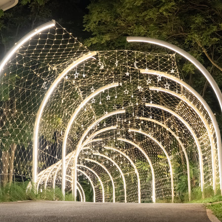 A curved tunnel lined with warm lights glows softly in the dark, and the illuminated arches guide the walkway through a quiet night scene.の写真素材