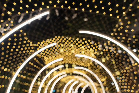 Warm golden bokeh fills the frame with soft circles of unfocused light, while curved LED lines create a bright tunnel effect in the background.の写真素材