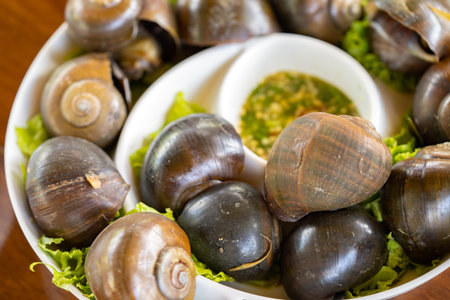 Brown shelled sweet snails Put them on a white platter alongside some more vegetables. Consume...