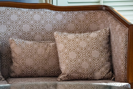 Sunlight shines on the elegant wooden sofa upholstered with ivory velvet fabric and a round coffee...
