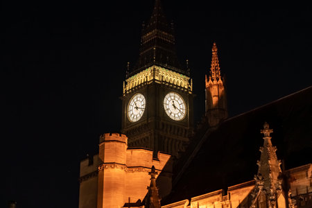 Close up Big Ben clock tower illuminated against a dark night sky. The iconic structure represents...