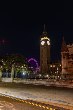 Big Ben clock tower seen from behind iron fencing at night. The layered view adds depth to London...