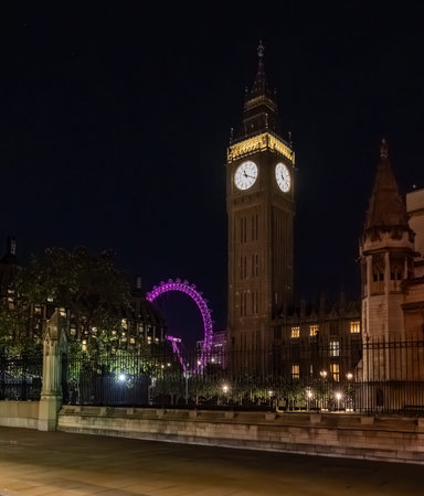 Big Ben clock tower seen from behind iron fencing at night. The layered view adds depth to London...