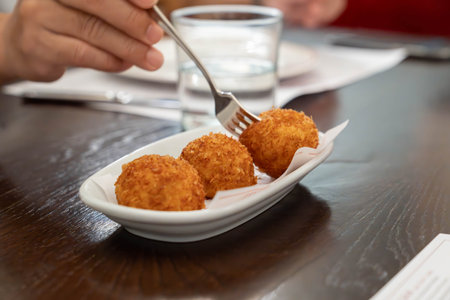 Golden crispy fried snack balls served on a small ceramic plate in a restaurant setting showing...