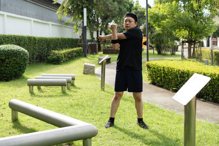 A man performs a cross-body shoulder stretch outdoors, focusing on warming up the deltoid and upper...