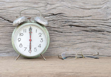 Old glasses and old green clock alarm on wood backgroundの写真素材