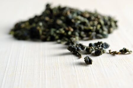Piles of dried green tea leaves isolated on wooden board background