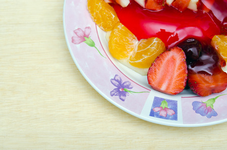 Strawberry jelly dessert flavored with half piece of strawberry, berry, and orange on the flower pattern dish top view with blank copy text space on wood backgroundの写真素材