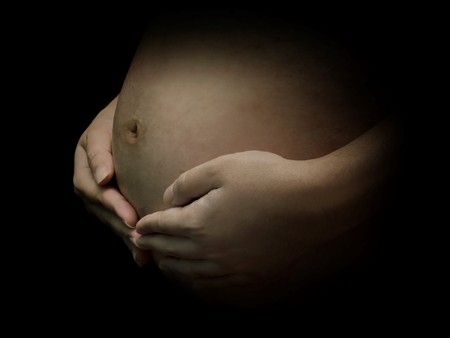 Pregnant woman with cute little baby inside and warm hand hold showing motherâs love and care with black backgroundの写真素材