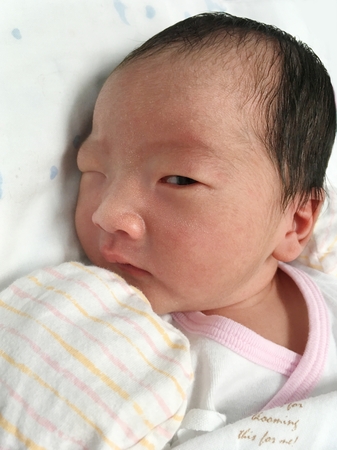 Little cute Asian girl baby lying on the bed is staring with one eyeの写真素材